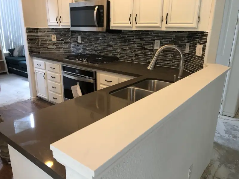 Peninsula kitchen with quartz counters and glass tile backsplash